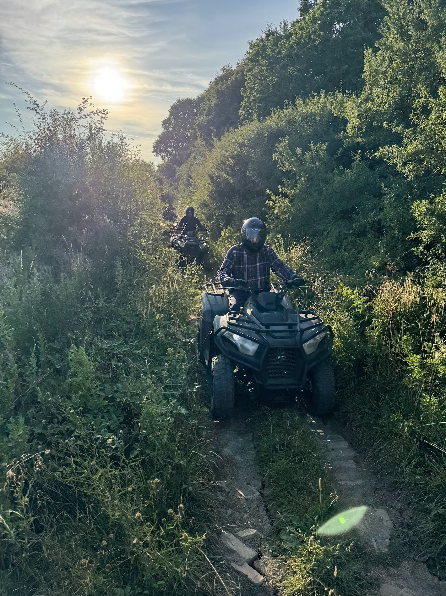 Riders on quad bikes navigating a narrow off-road trail through Yorkshire countryside at golden hour